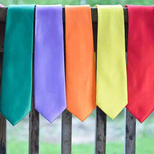 Five bright solid color neckties hanging on a wooden railing outdoors.